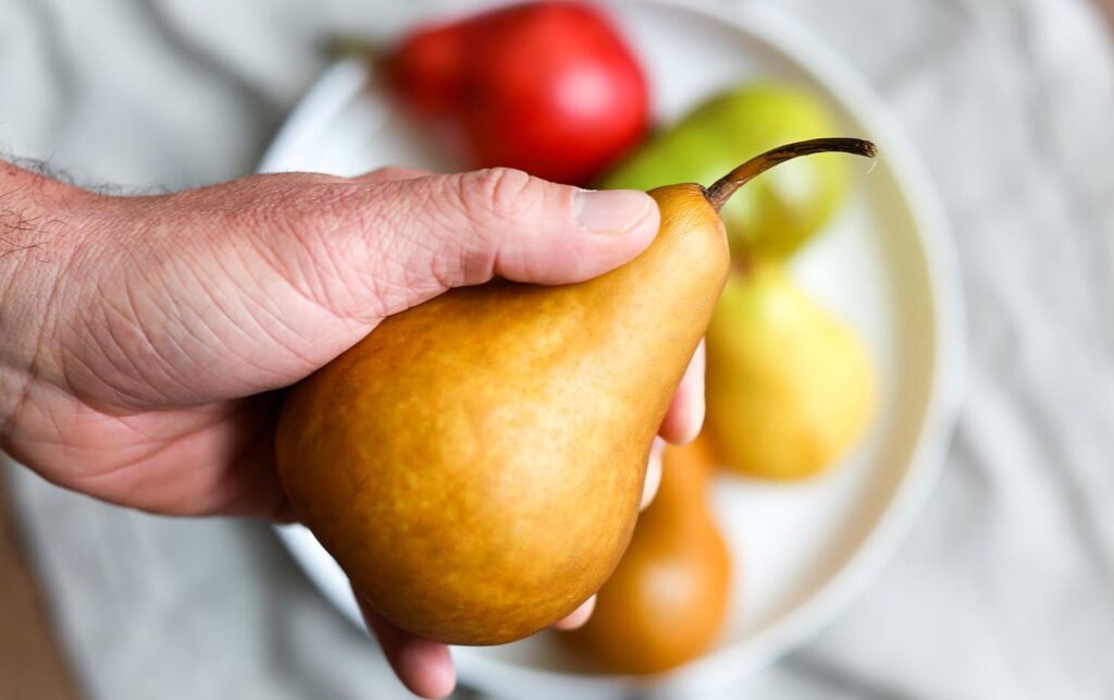 A hand holding a pear and below it is a plate with more pears.