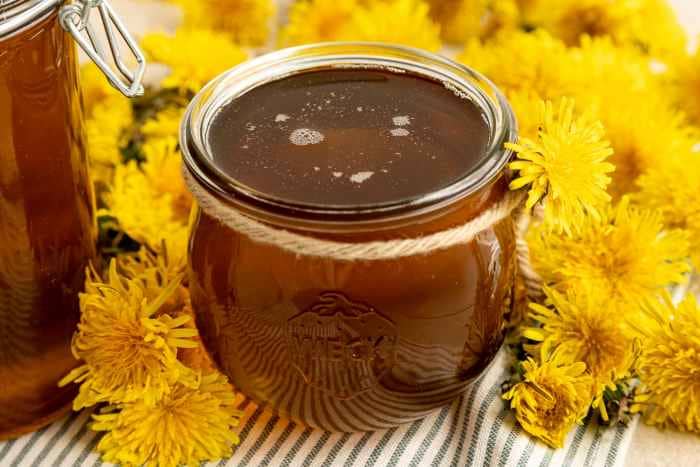 Jar with dandelion honey and dandelion flowers.