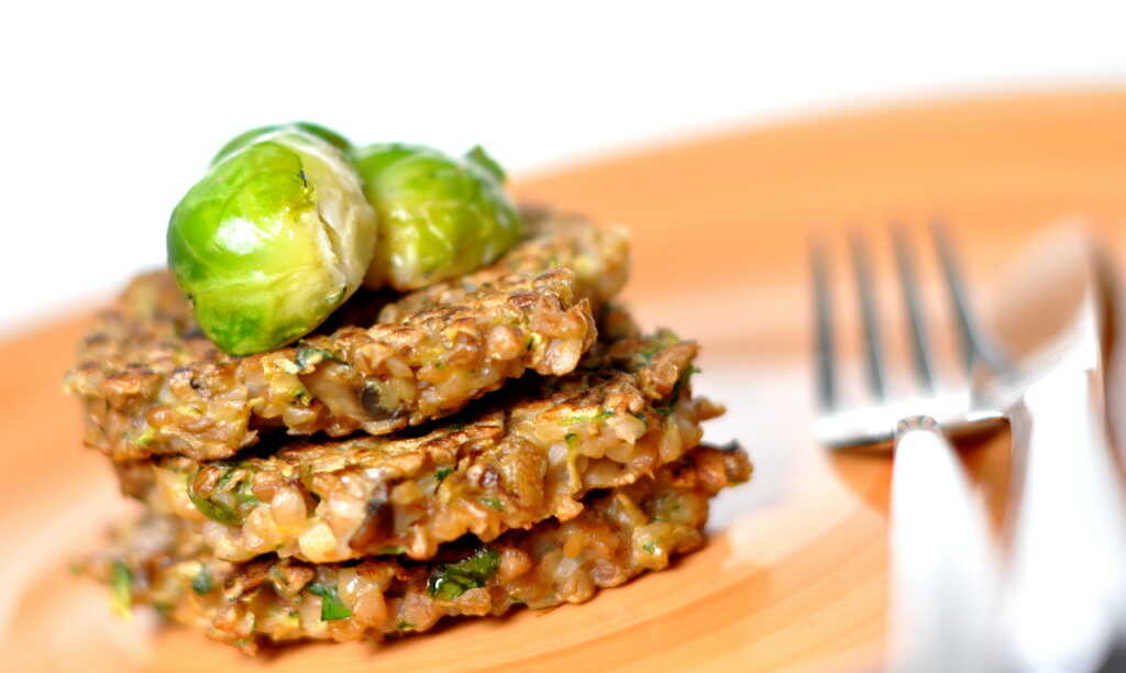 Buckwheat patties stacked on top of each other, decorated with Brussels sprouts and served on a plate with cutlery.
