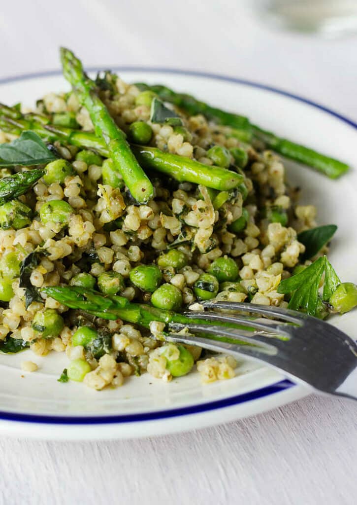 Buckwheat risotto with asparagus, peas and basil on a plate with a fork.