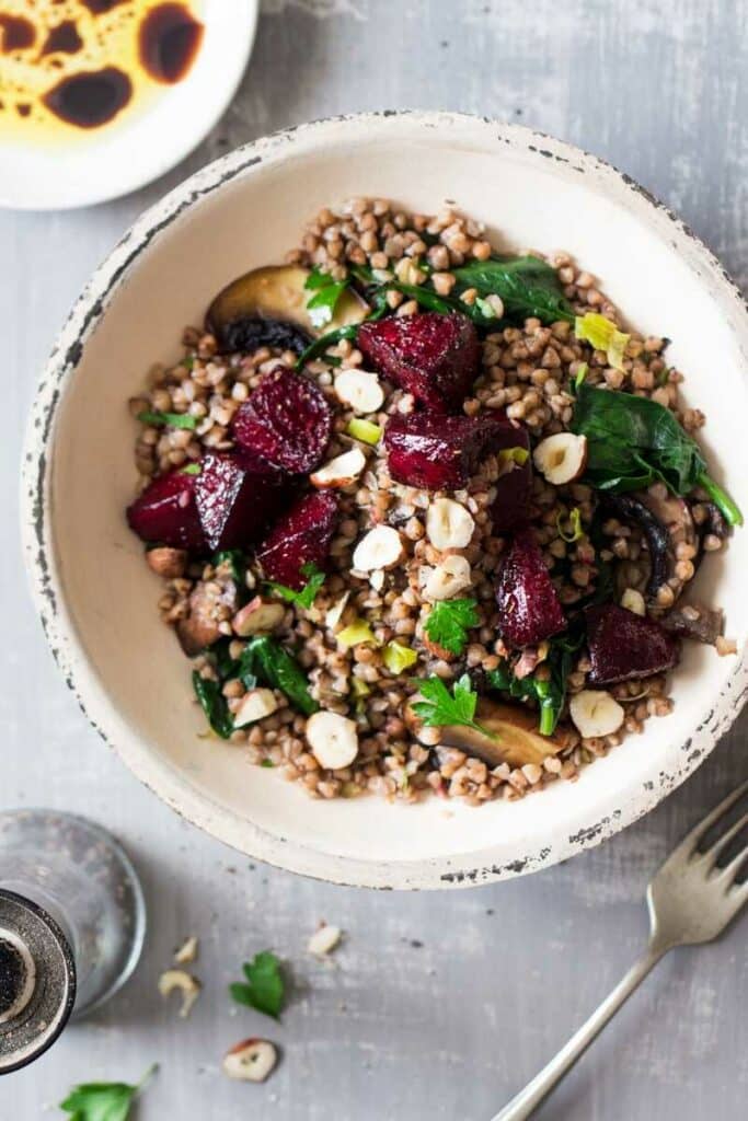 Buckwheat with pieces of roasted beetroot, nuts, vegetables and fresh herbs in a deep plate.