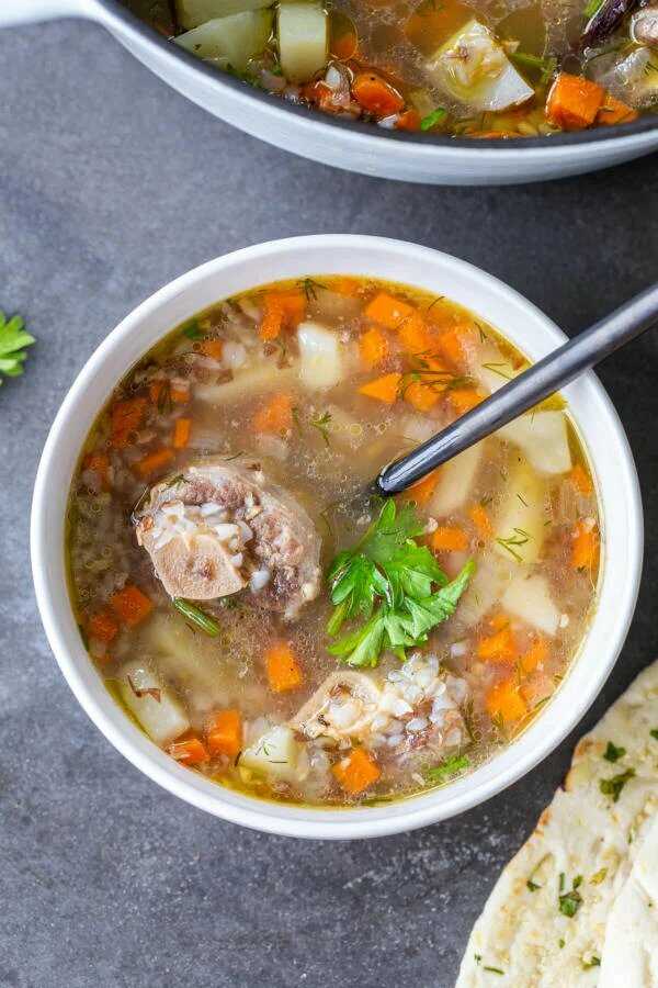 Ein tiefer Teller voller Suppe mit Gemüse, Fleisch, Buchweizen und frischen Kräutern.