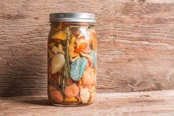 Pickled mushrooms with vegetables and herbs in a mason jar.