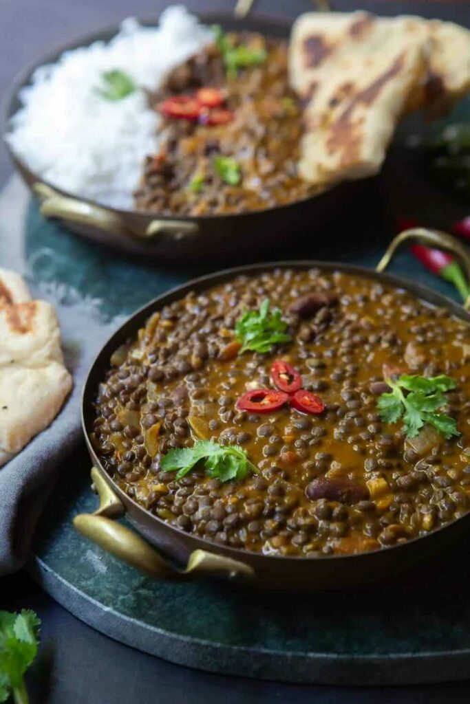 Curry de lentilha servido em uma panela e decorado com ervas e pimenta malagueta.