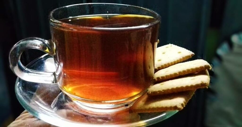 Čaj z cibule ve skleněném hrnečku na podtácku se sušenkami.