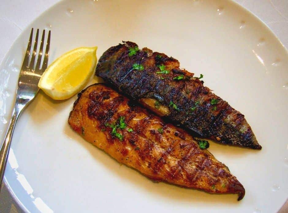 Grilovaná makrela servírovaná na talíři s klínkem citronu a vidličkou.