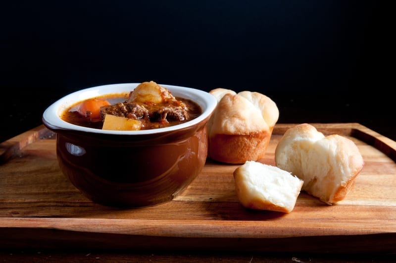 Goulash made of lamb, vegetables and black olives served in a small bowl with pastry on the side.