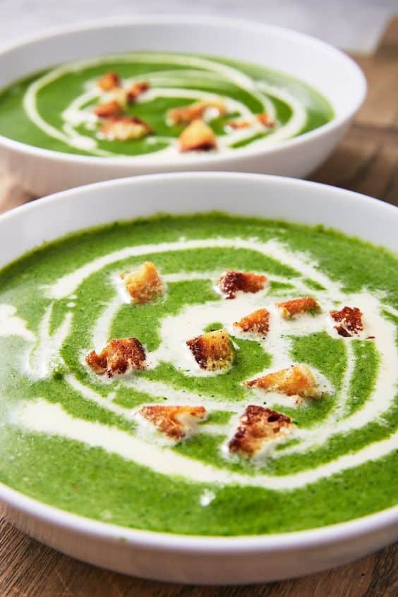 Miska plná zelené polévky z čerstvého špenátu s krutony a zakysanou smetanou.
