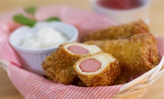 Fried rolls filled with sausage served in a cup with a bowl of dip.