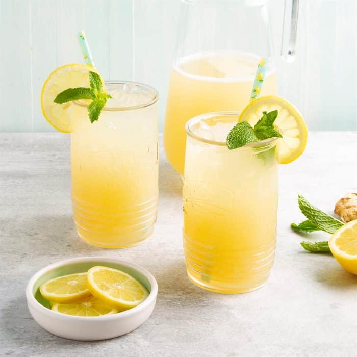 Limonáda ze zázvoru ve sklenicích s brčkem, ozdobená čerstvou mátou a plátkem citronu. 
