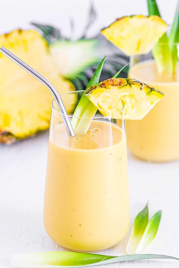 Ovocné smoothie ve sklenici s brčkem ozdobené plátkem ananasu.