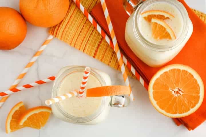 Ovocené smoothie ve sklenicích s brčky ozdobené pomeranči a vedle jsou položené čerstvé pomeranče.