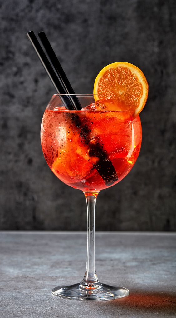 Ein randvoll gefülltes Weinglas mit einem süßen Cocktail aus Aperol und Orangen.