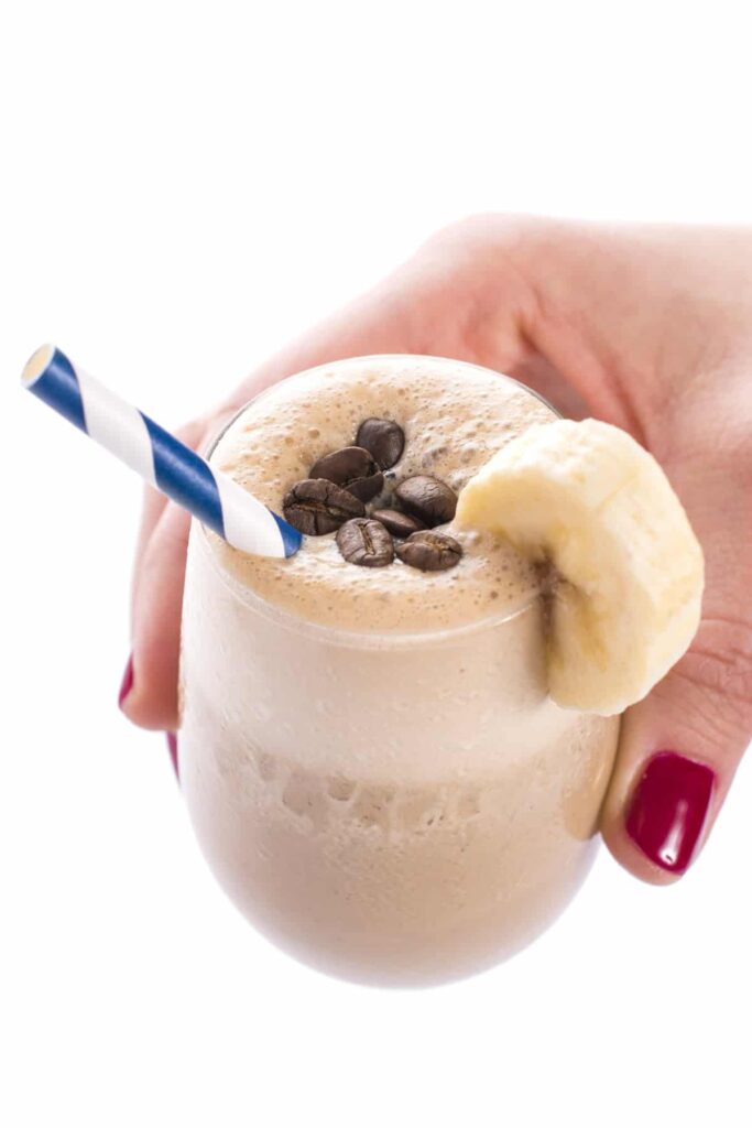 Smoothie z banánu a kávy ve sklenici s brčkem, kterou drží ruka. 
