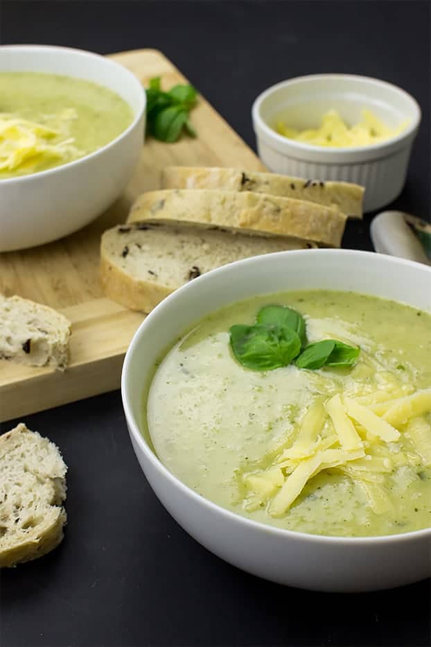 Květákovo-brokolicová polévka servírovaná v miskách, ozdobená strouhaným sýrem a čerstvou bylinkou. Vedle je nakrájený čerstvý chléb.
