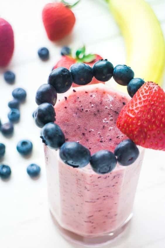 A pink drink made of blueberries and strawberries decorated with the same fruit.