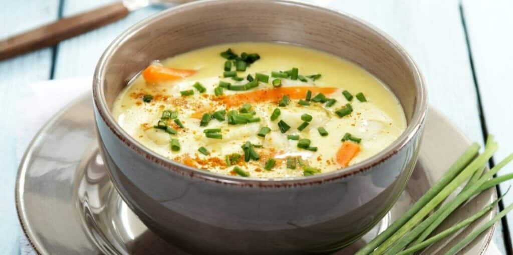 Krémová polévka z ryb servírovaná v mističce a ozdobená pažitkou.
