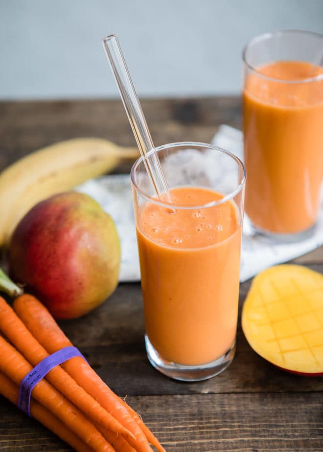 Ovocno-zeleninové smoothie ve sklenici s brčkem s vedle položenou mrkví, mangem a banánem.