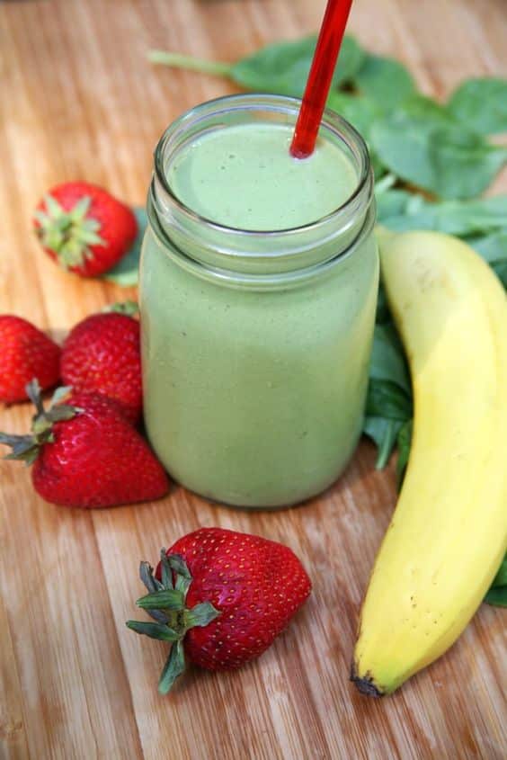 A glass with a drink made of spinach, banana and strawberries.