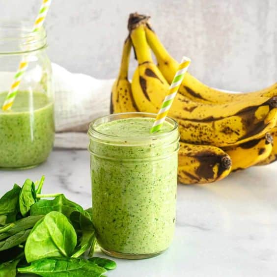 A glass with mixed spinach, banana and carrot.