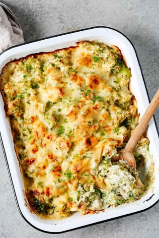 Baked vegetables with chicken in a baking dish with a wooden spoon.