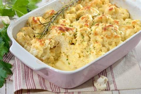 Cauliflower gratin with cheese in a baking dish, decorated with a sprig of rosemary.
