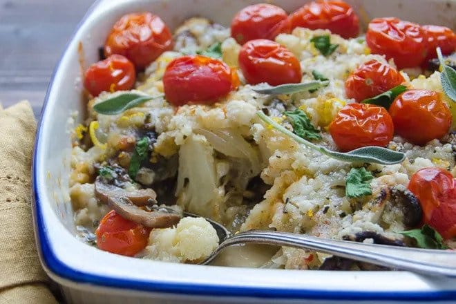 Cauliflower gratin with mushrooms and tomatoes in a baking dish with a spoon.