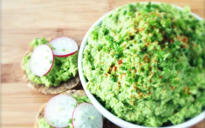 Avocado-pea spread in a bowl. On the side are buttered buns and garnished with radish.