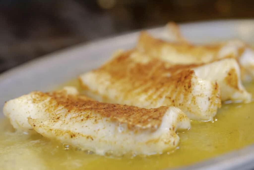 Baked white fish on a plate, topped with sauce.