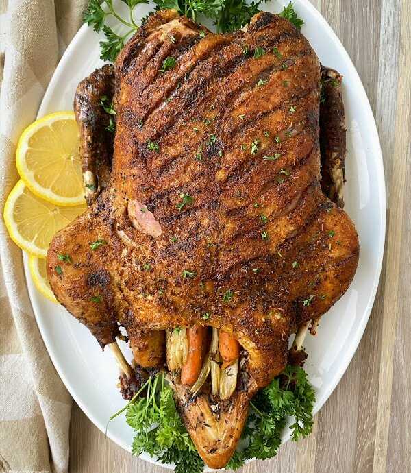 A whole duck stuffed with vegetables on a large plate, garnished with fresh herbs and lemon slices.
