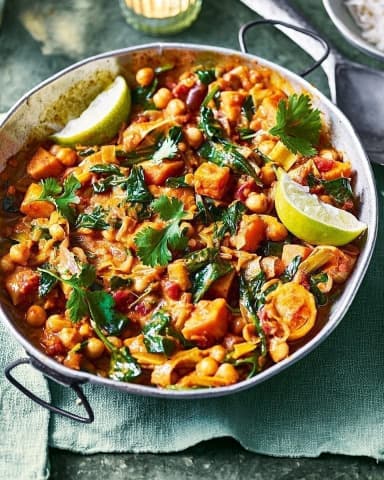 Legume-vegetable curry in a pan, garnished with fresh coriander and lime wedges.