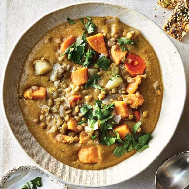 Linsen-Gemüse-Suppe in einem tiefen Teller serviert und mit frischen Kräutern garniert.