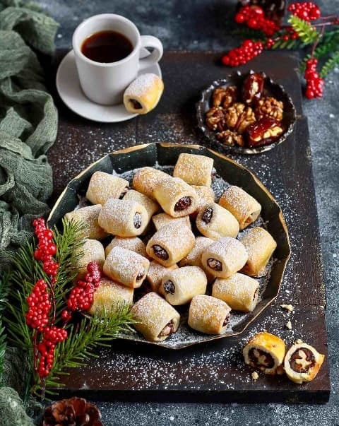 Stuffed butter rolls on a festive tray. A mug with coffee and a bowl of nuts are placed next to it.