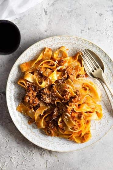 Pasta with pieces of duck meat and cheese on a plate with a fork.