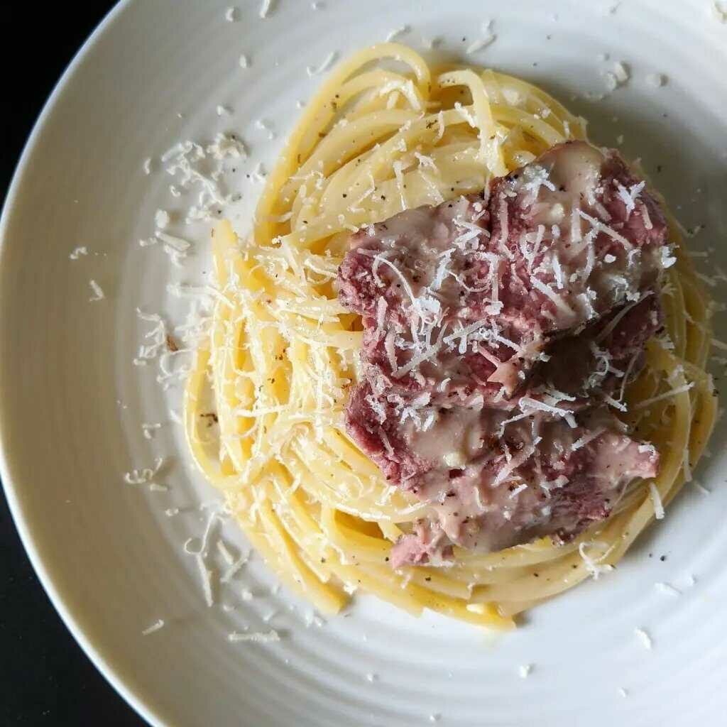 Spaghetti with duck meat on a plate, sprinkled with cheese.