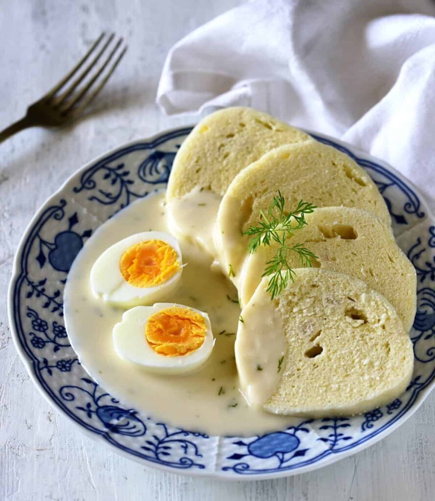 Smetanová omáčka s koprem servírovaná na talíři s vejcem a houskovým knedlíkem.