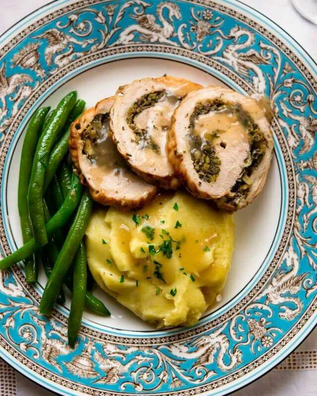 Roll filled with mushrooms and leeks served on a plate with mashed potatoes and green beans.