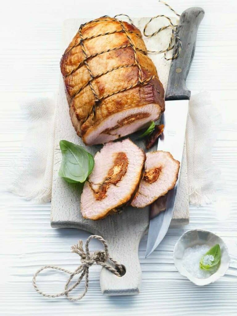 Turkey roll stuffed with basil, cheese and tomatoes on a wooden board with a knife.