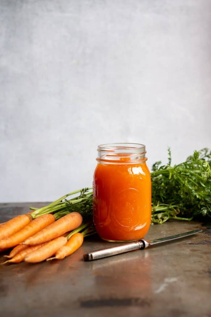 Karottenmarmelade in einem Glas und frische Karotten und ein Messer werden daneben gestellt.
