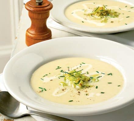 Krémová polévka z pórku servírovaná v hlubokých talířích, ozdobená pórkem a pažitkou.