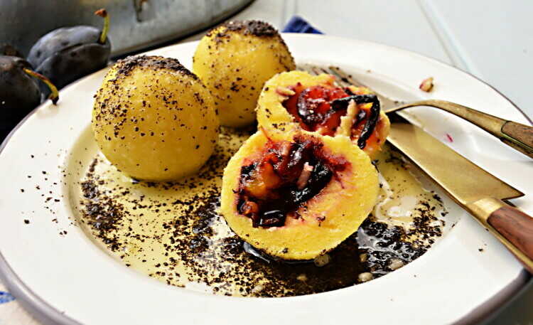 Plum dumplings on a plate with cutlery, sprinkled with poppy seeds.