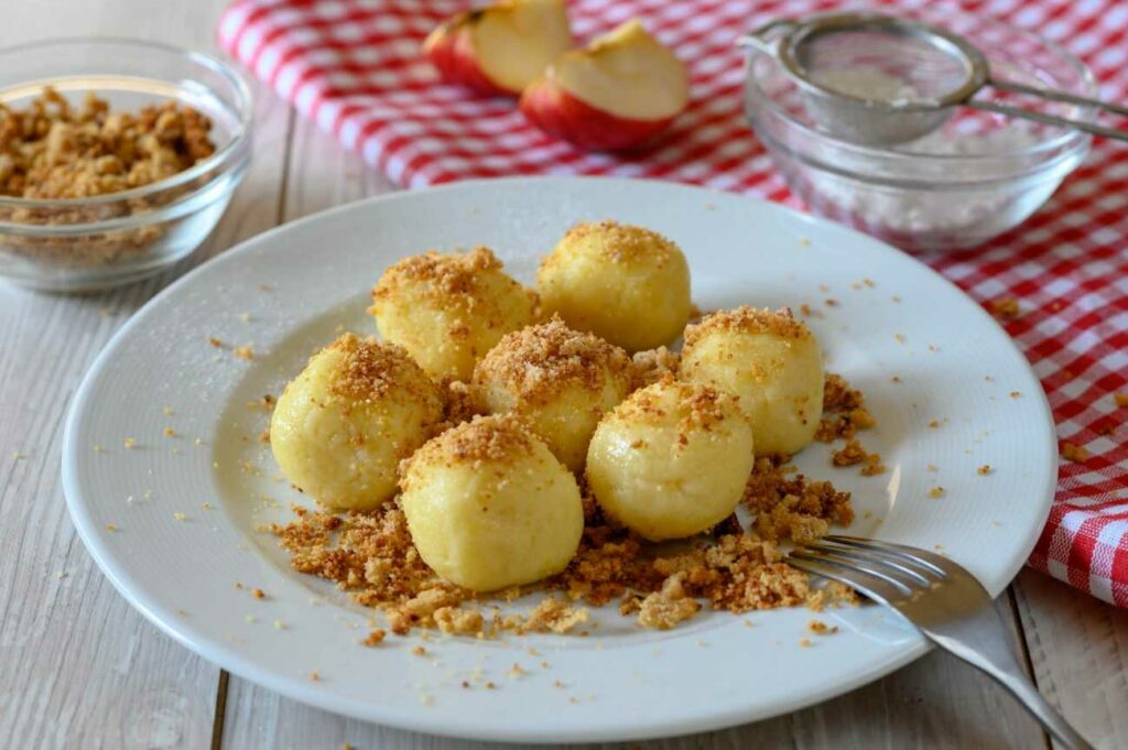 Potato dumplings with fruit served on a plate with a fork and sprinkled with breadcrumbs.