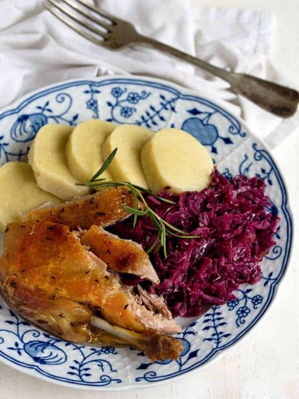 Kus kachny s bramborovým knedlíkem a červeným zelím na talíři s vedle položenou vidličkou.
