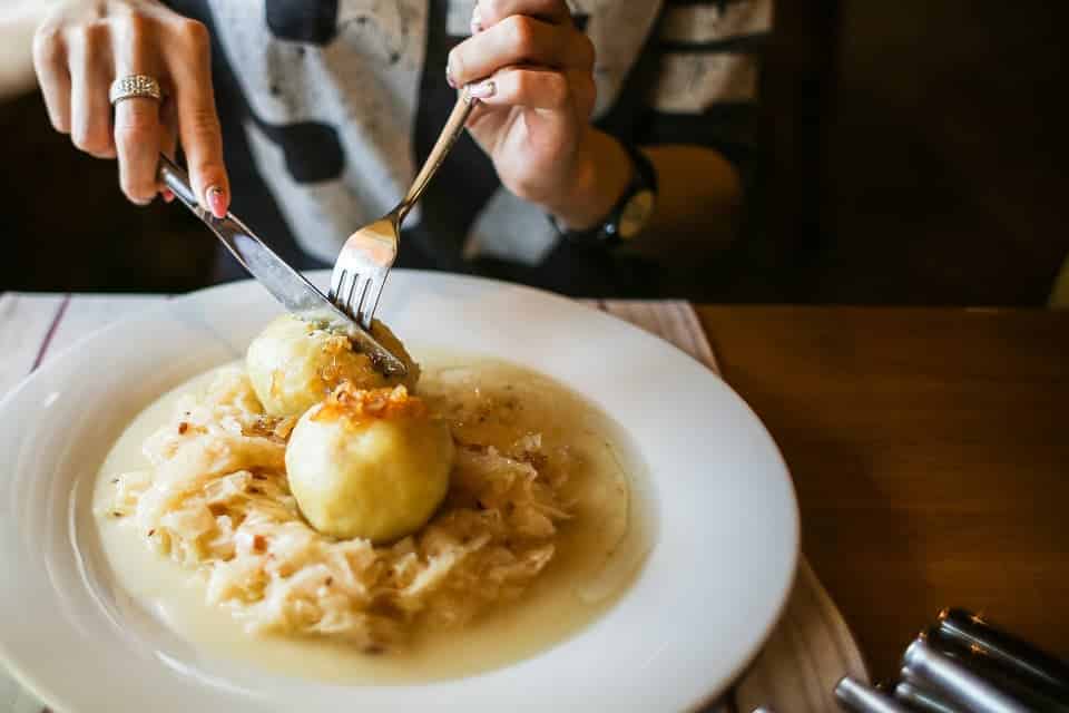 Potato dumplings on a plate with steamed cabbage being cut by a woman.