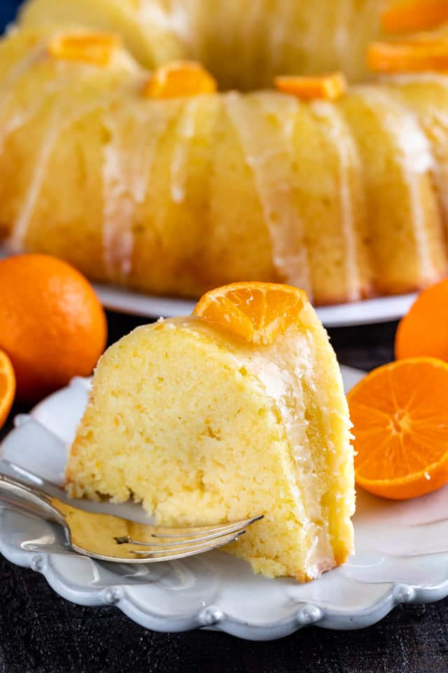 A piece of sponge cake on a plate with a fork and fresh oranges.