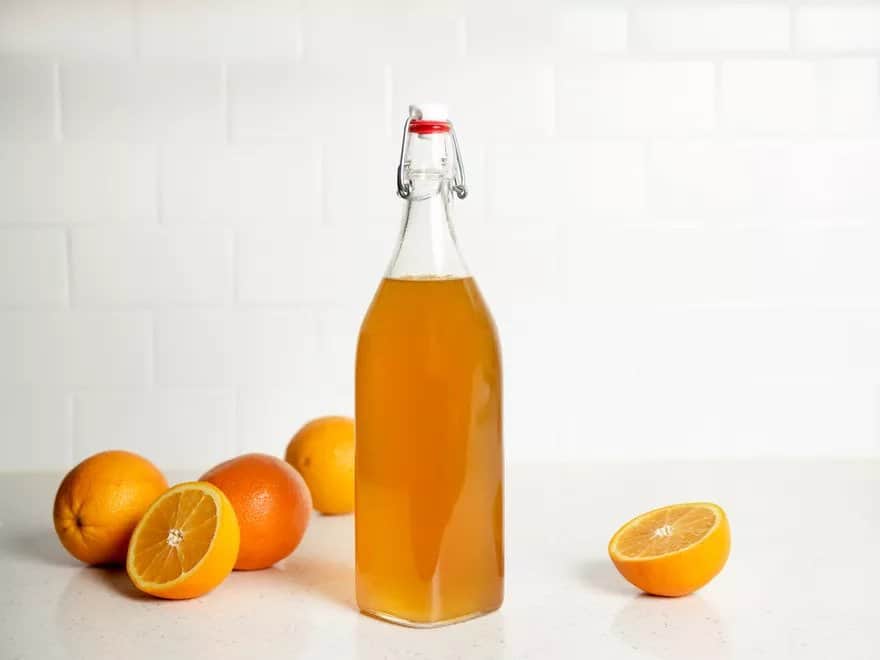 Orange liqueur in a glass bottle and fresh oranges are placed next to it.