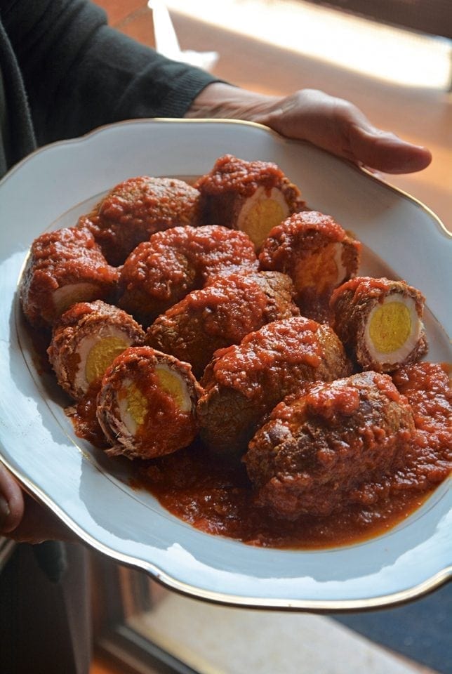 Meat rolls filled with eggs, served on a plate and topped with tomato sauce.