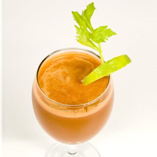 A vegetable smoothie in a glass with a lime wedge and a celery leaf.