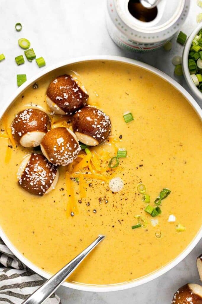 Cheese and beer soup in a deep plate with a spoon, garnished with cheese, spring onions and soft pretzels.