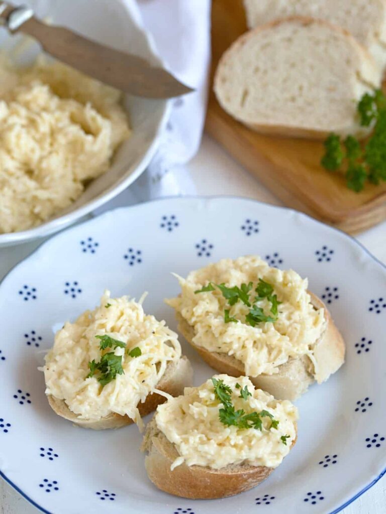 Roll slices smeared with cheese and garlic spread, garnished with chopped parsley and served on a plate.